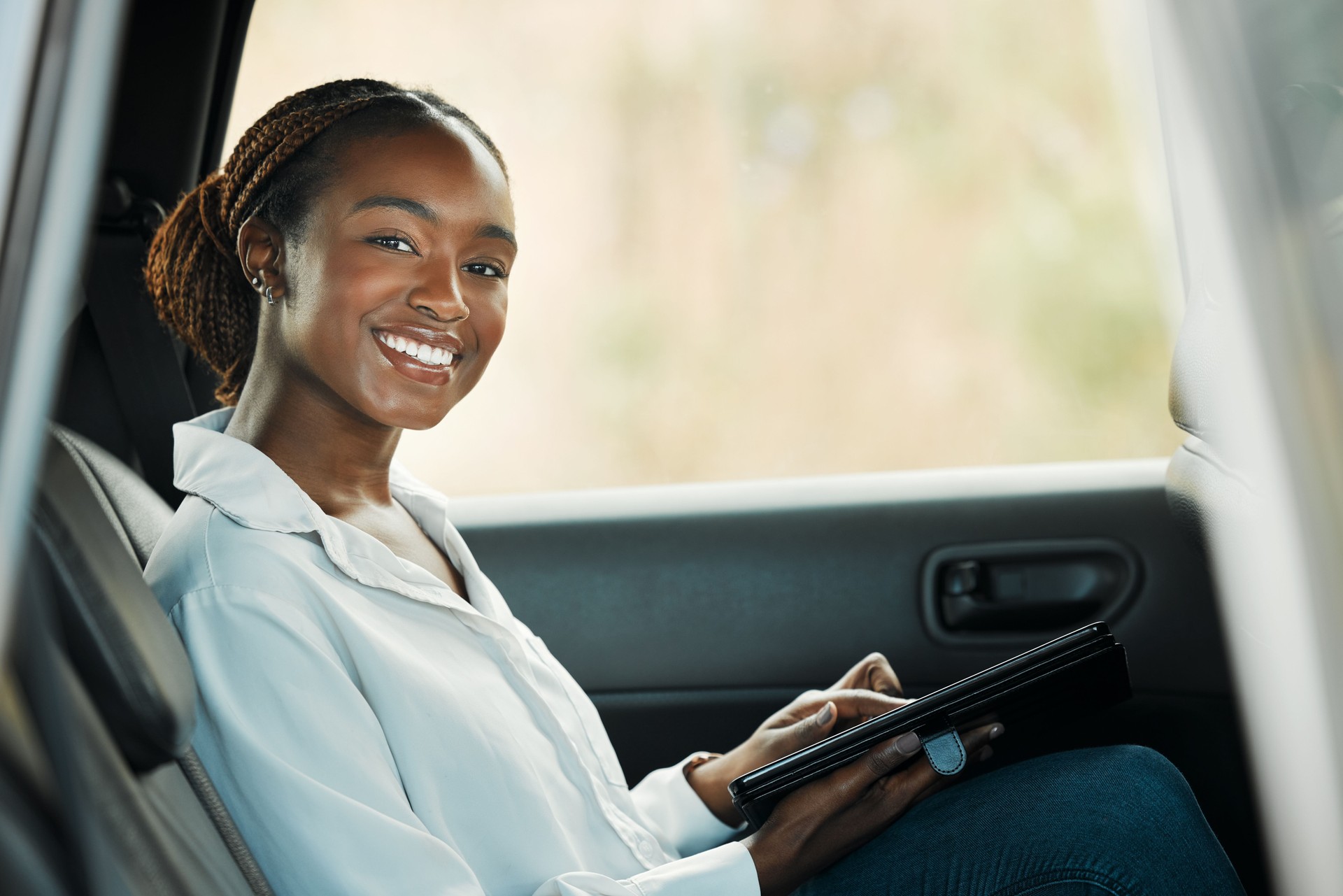 Portrait, tablet and a business black woman a taxi for transport or ride share on her commute to work. Smile, technology and a happy young employee in the backseat of a cab for travel as a passenger